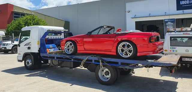 Red convertible secured on the blue tilt tray outside a workshop