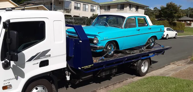 Turquoise Holden EK strapped to the blue tilt tray on a residential street