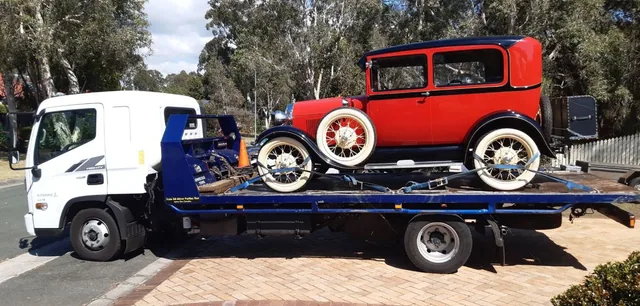 Red and black vintage sedan with cream wire wheels strapped to the tilt tray on a driveway